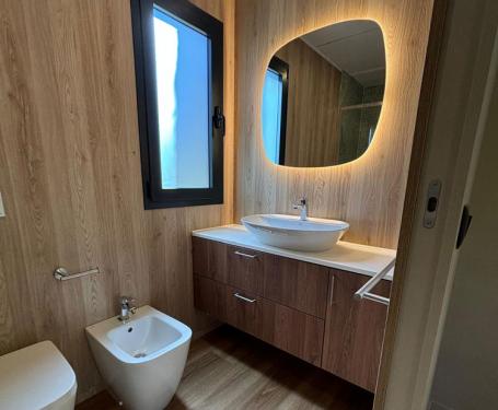 Modernes Badezimmer mit Waschbecken, Bidet, Toilette und beleuchtetem Spiegel.