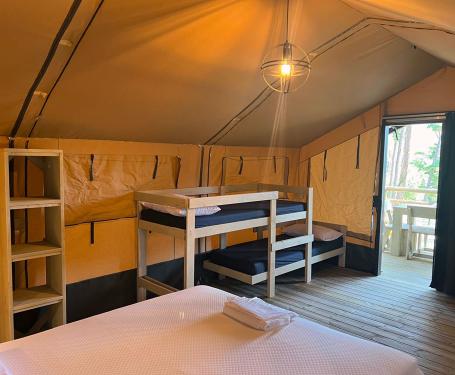 Tenda glamping con letti a castello e matrimoniale, arredi in legno, veranda esterna.