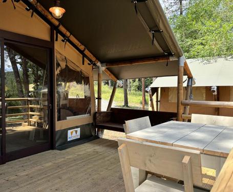 Glamping-Zelt mit Veranda, Holztisch und Stühlen inmitten der Natur.